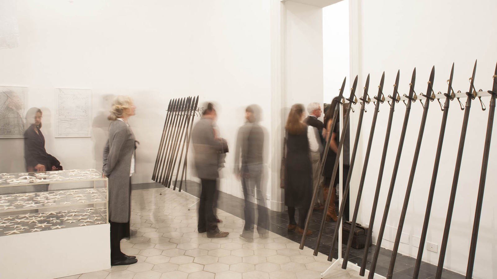 Installation view of Terry Adkins's work &quot;Meteor Shower&quot; at AAR in 2015, showing people milling about a room with pikes (pole weapons) leaning on the wall in a row