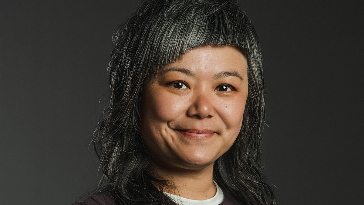 Color photograph of an Asian woman with black and gray hair smiling at the camera