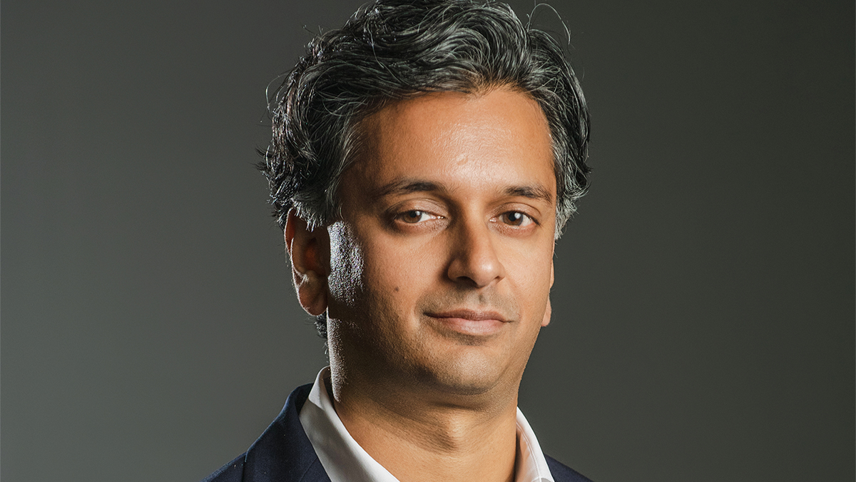 Rome Prize Fellows - Ajay Manthripragada Color photograph of an olive skinned man wearing a collared shirt and dark blazer looking at the camera with a serious expression