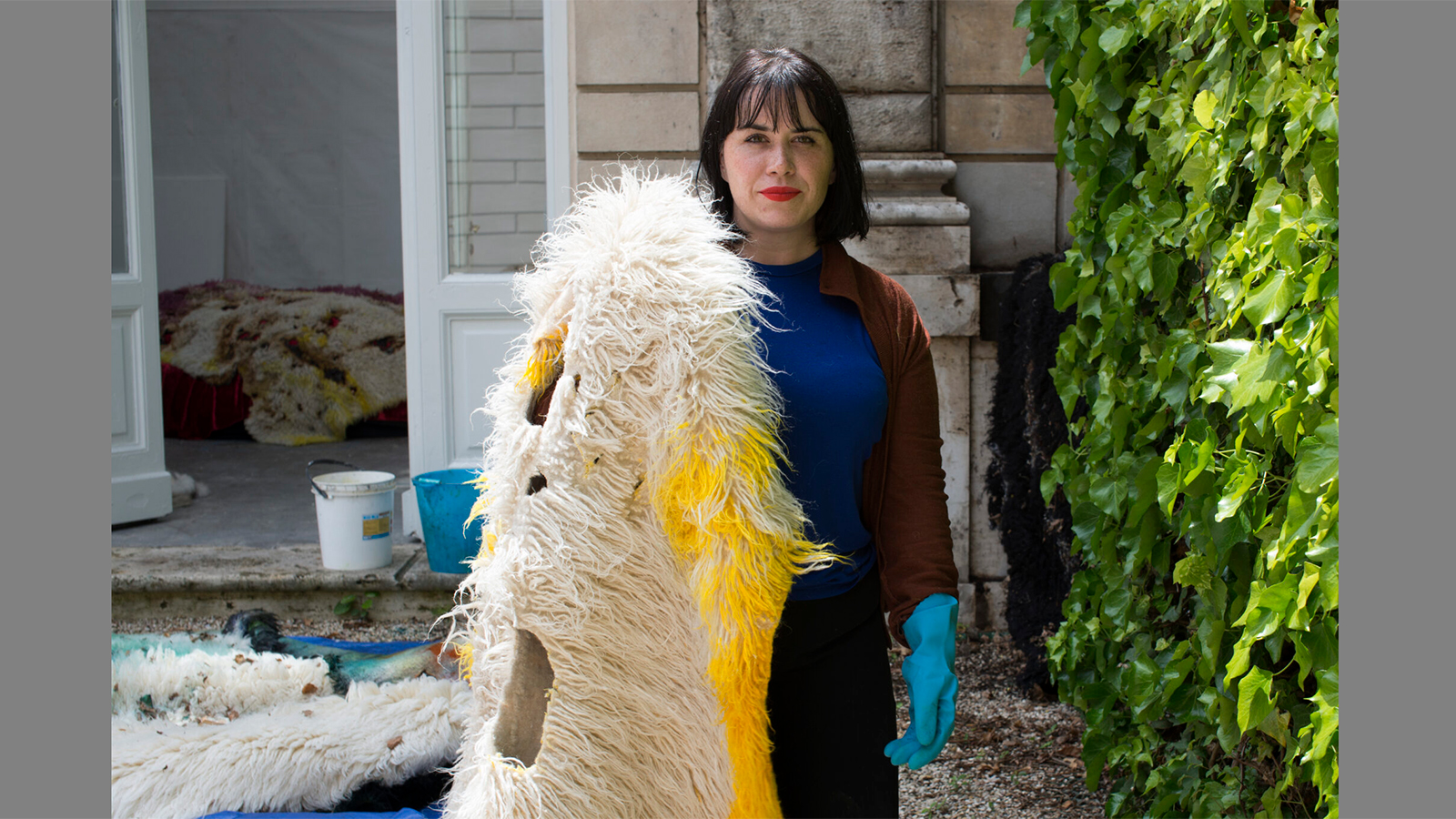 Color photo of light skinned woman with dark hair holding a flotaki rug that has been burned and dyed