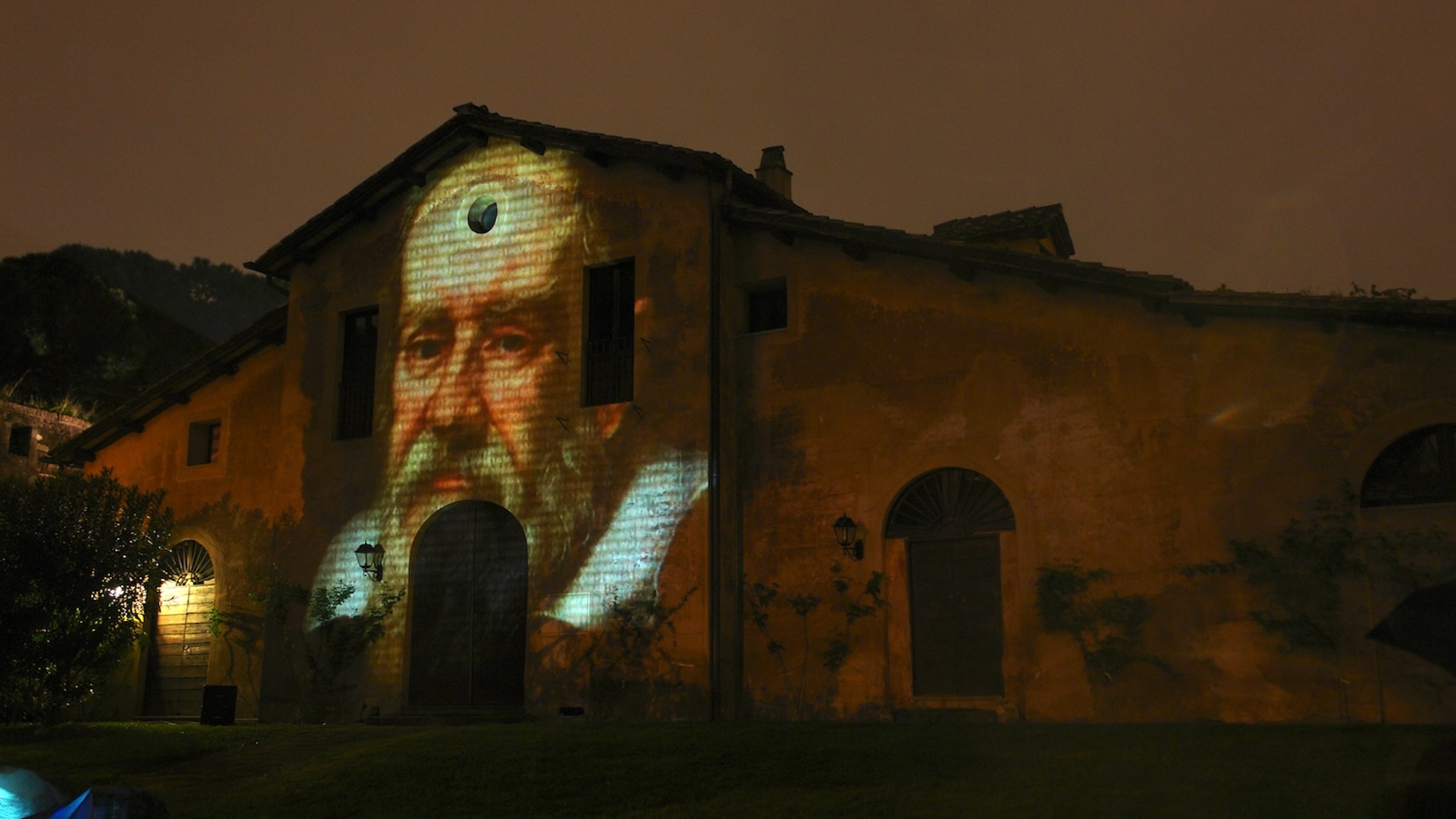 A projected image of Galileo on the face of an old building, dusk