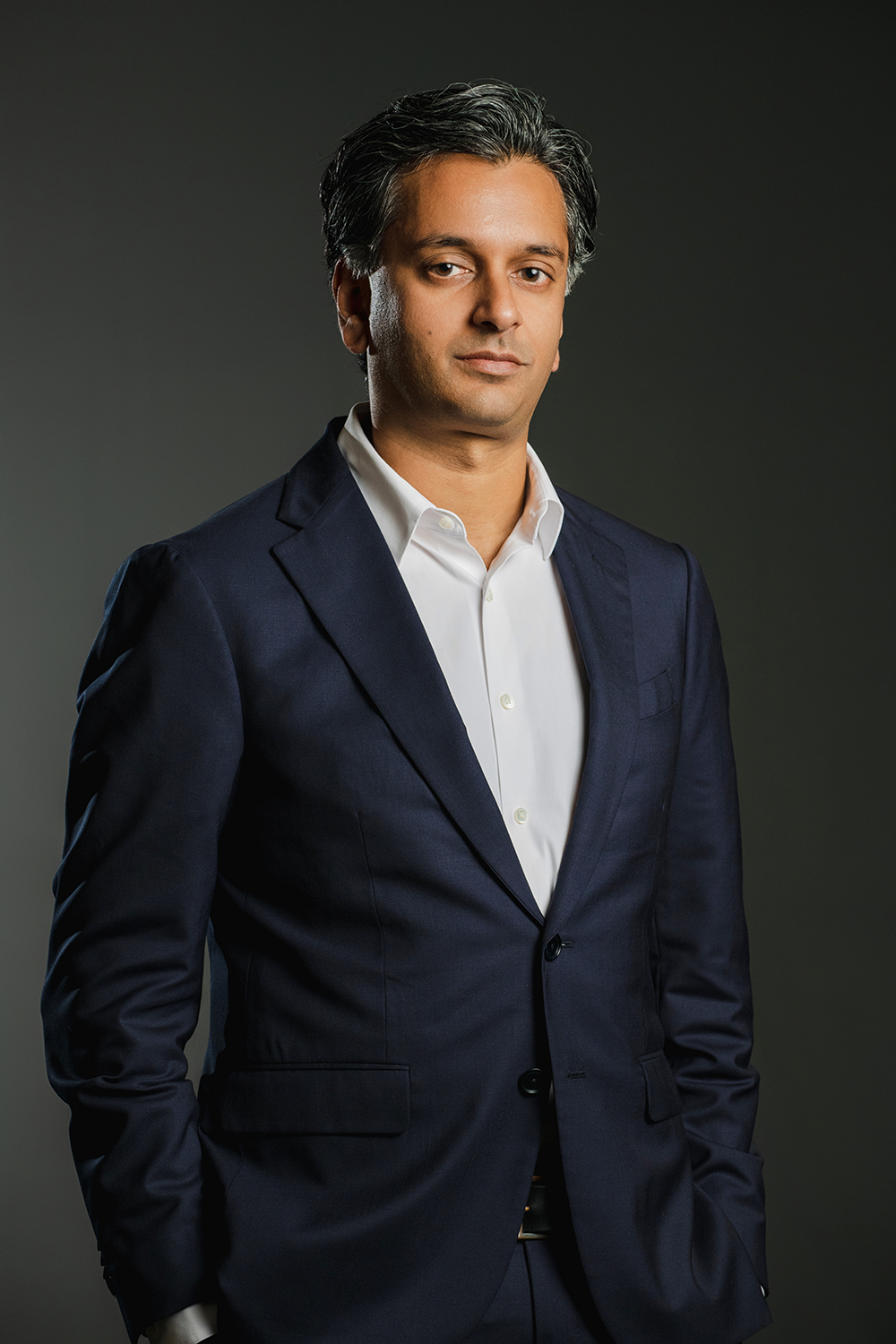 Ajay Manthripragada Color photograph of an olive skinned man wearing a collared shirt and dark blazer looking at the camera with a serious expression