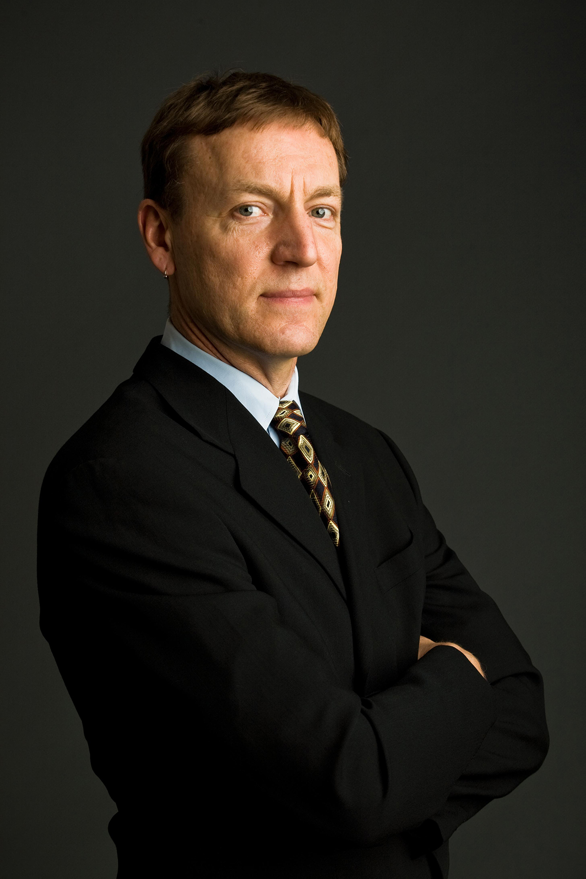 David Humphrey Color photograph of the head and torso of a light skinned man in a photographer's studio wearing a dark suit and tie and looking at the camera with a serious expression