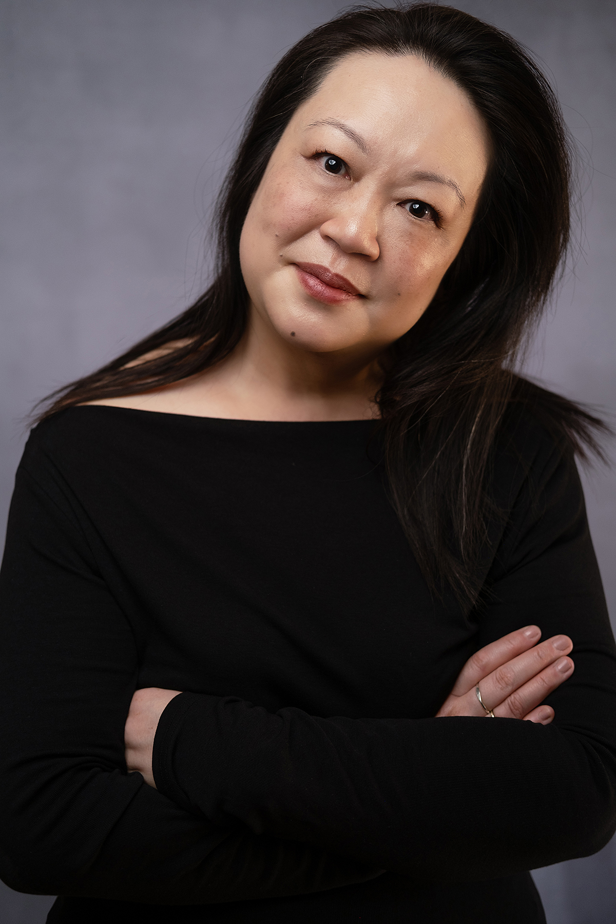 Staff - Aliza Wong A color photograph of the head and torso of an Asian woman; she tilts her head to the left while looking directly at the camera