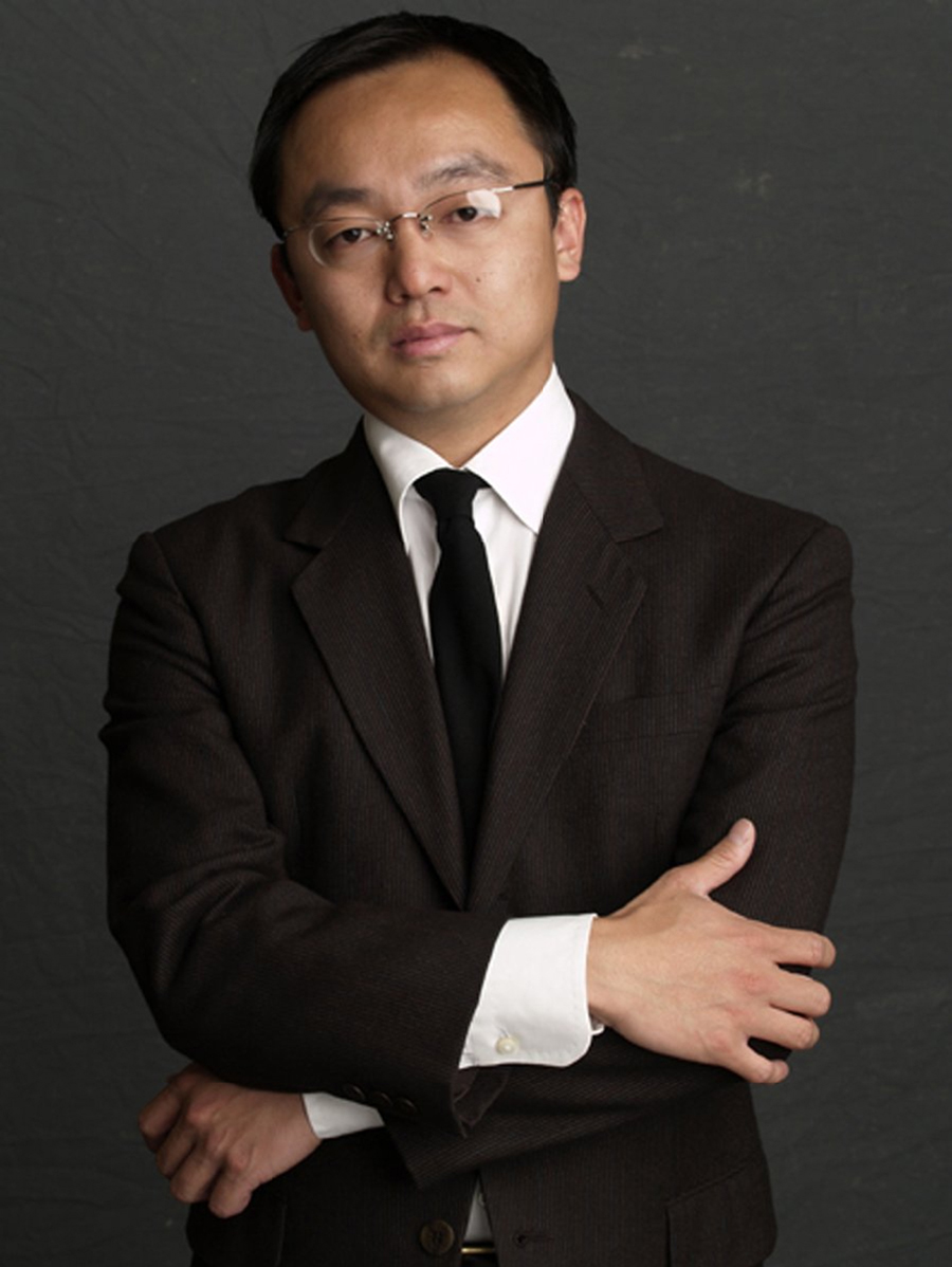 Thomas Tsang Color photograph of the head and torso of an Asian man wearing a dark suit, crossing his arms across his stomach, and looking at the camera in a serious manner