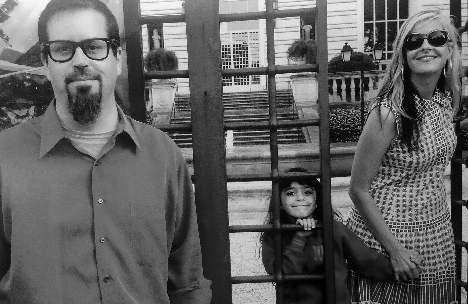 Black and white photograph of the heads and torsos of a light skinned man, child, and woman in front of an iron gate at the American Academy in Rome