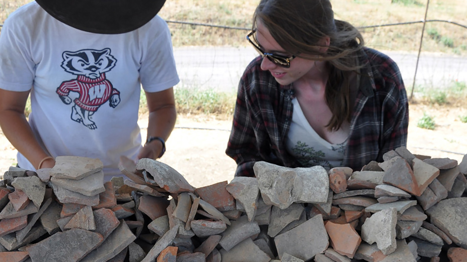 Two Summer School participants stand next to and examine dozens of fragments of ancient Roman pottery