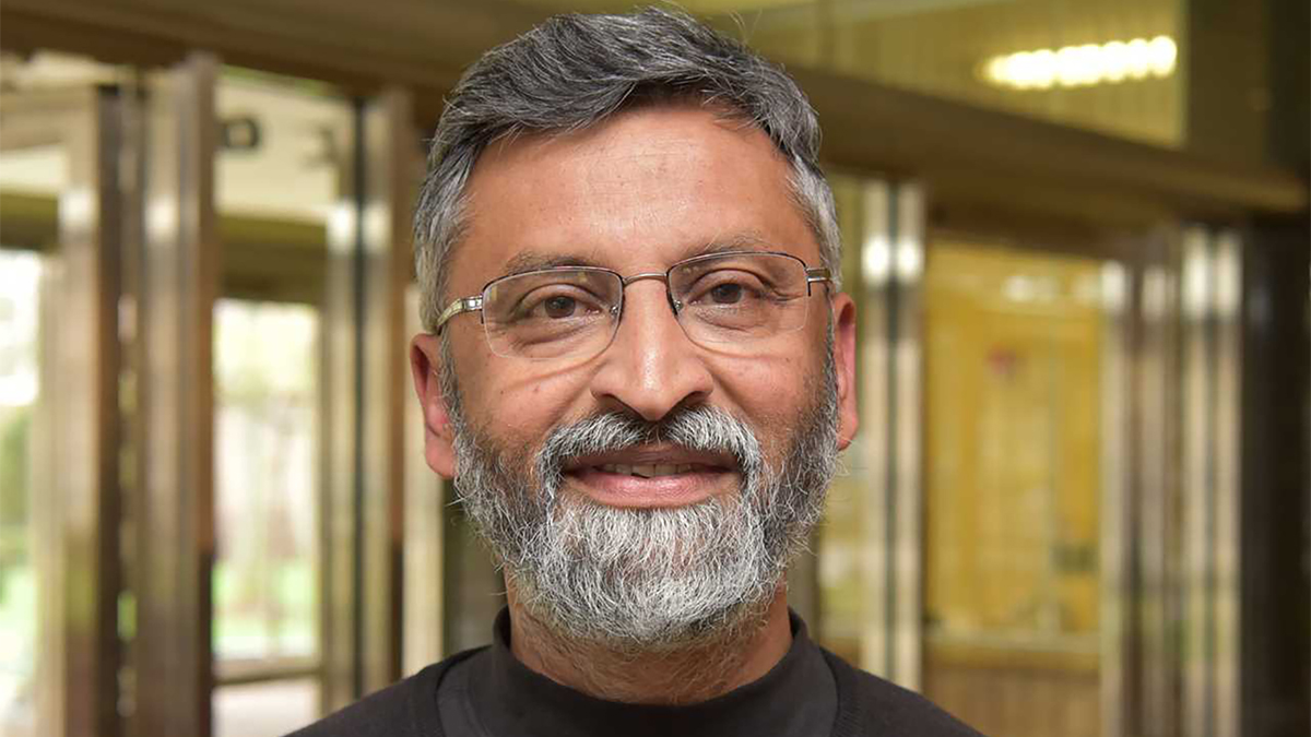 Color photo of the face of a gray bearded Indian man smiling slightly