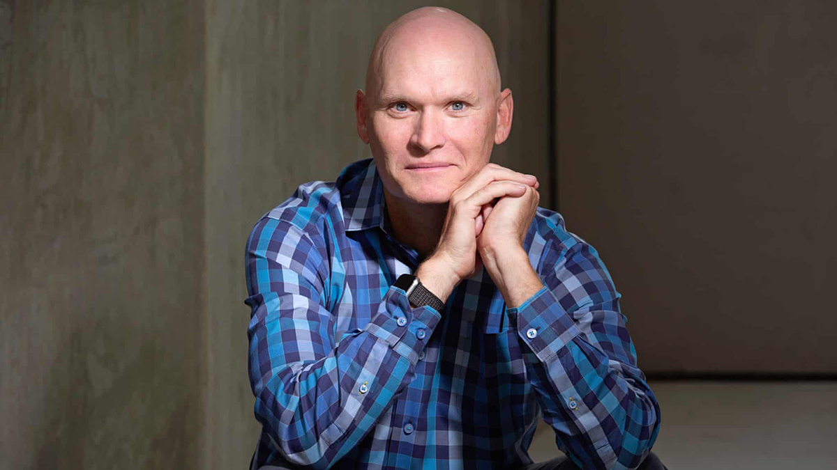 Color photograph of the torso of Anthony Doerr, wearing a checkered shirt with his chin resting on raised arms