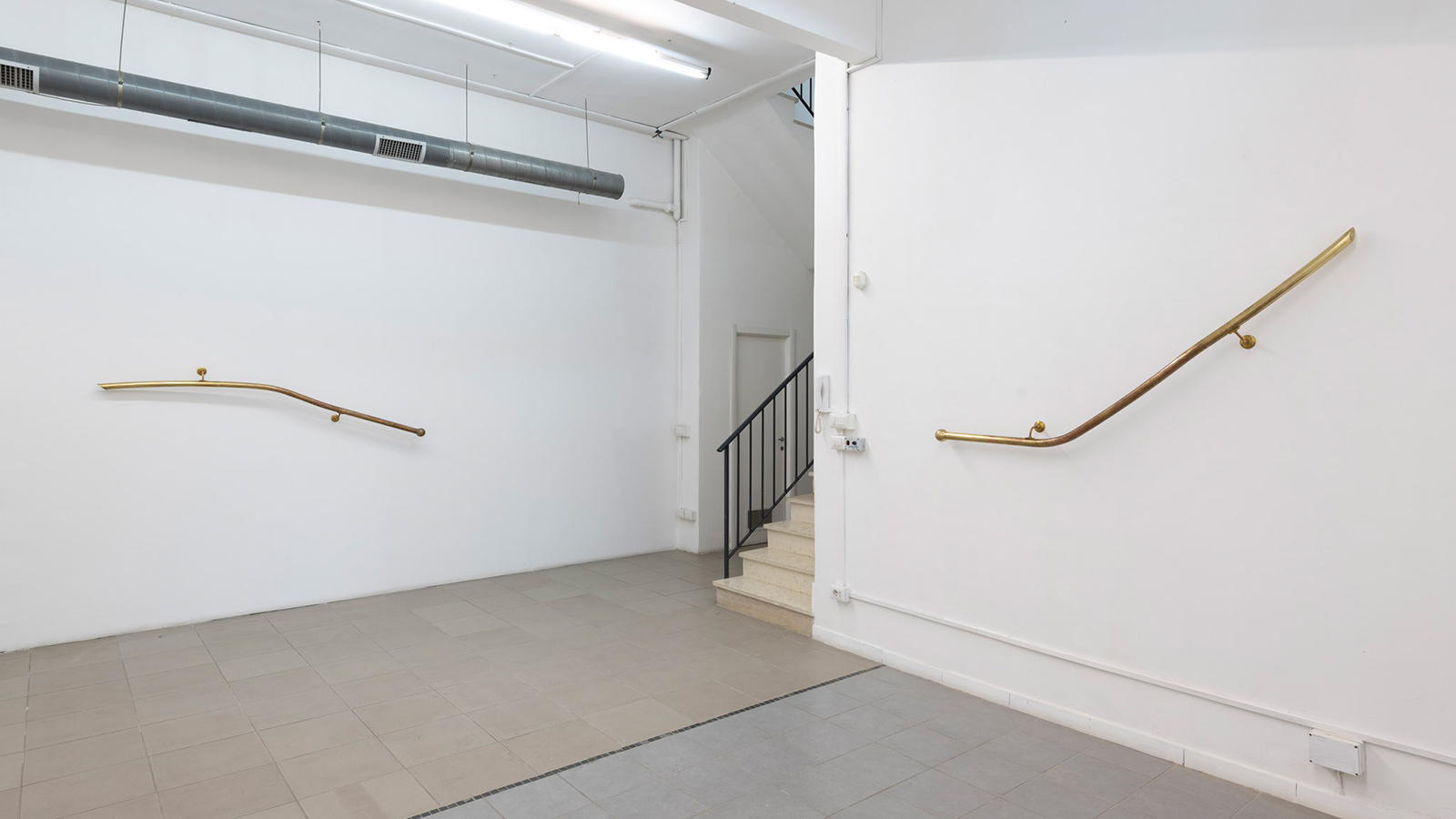 Color photograph of an installation view of two oxidized brass handrail sculptures by Corinna Gosmaro, attached to the gallery walls