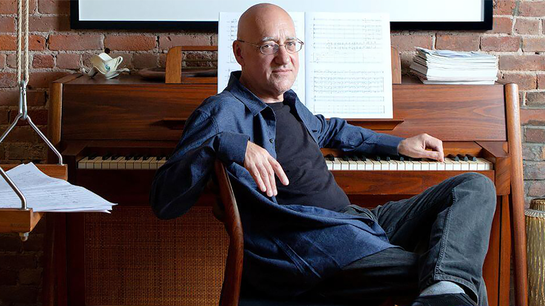 Color photograph of a white man sitting at a piano, looking at the camera