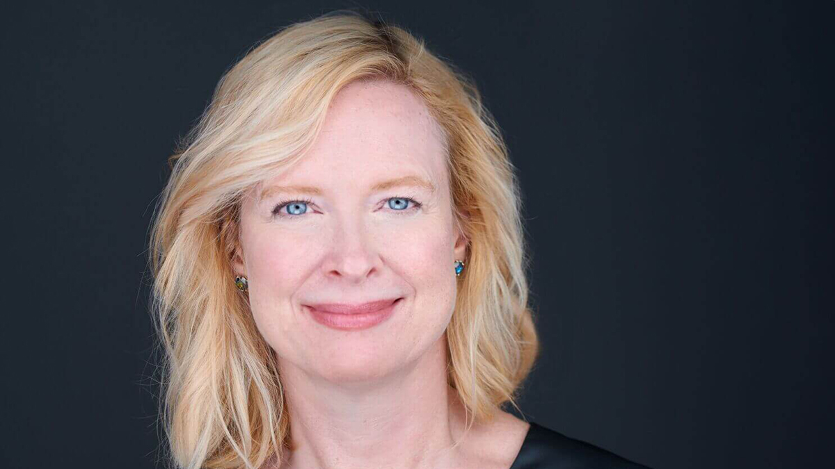 Color photograph of the smiling face of a light skinned woman with blond hair