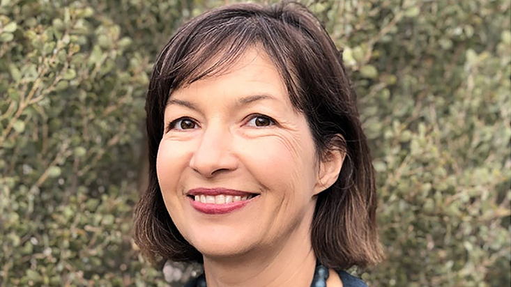 Color photograph of the face of Emma Blake in front of green foliage
