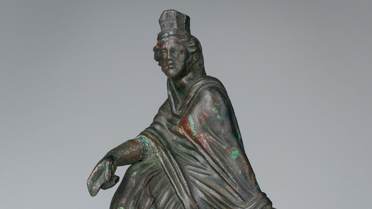 Color photograph showing a detail of a small bronze statute of a seated woman wearing a toga
