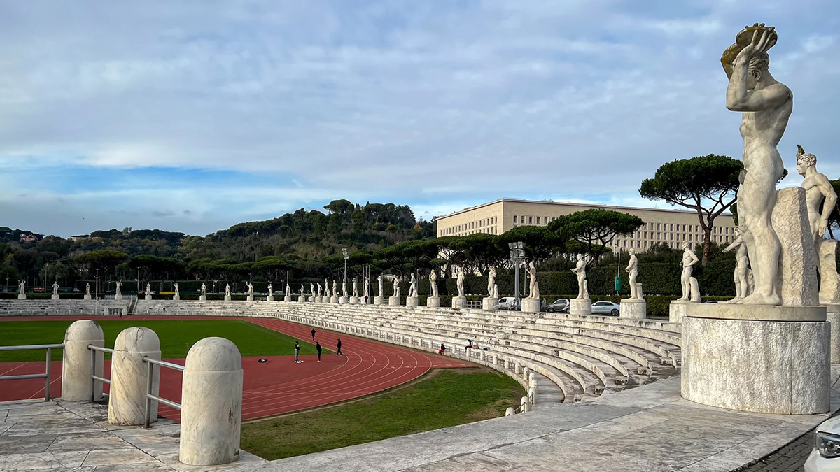 Color photograph of a modern sports track in Italy surrounded by stone statues of athletes