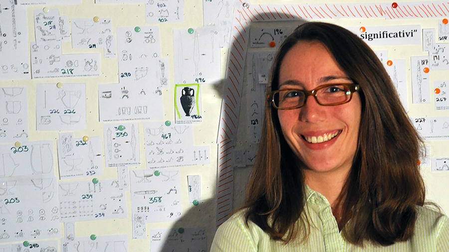 Color photo of the head and shoulders of a light skinned woman wearing glasses and smiling at the camera