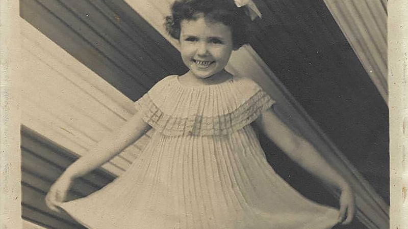 Sepia toned photo of a young light skinned girl courtseying in a light colored dress