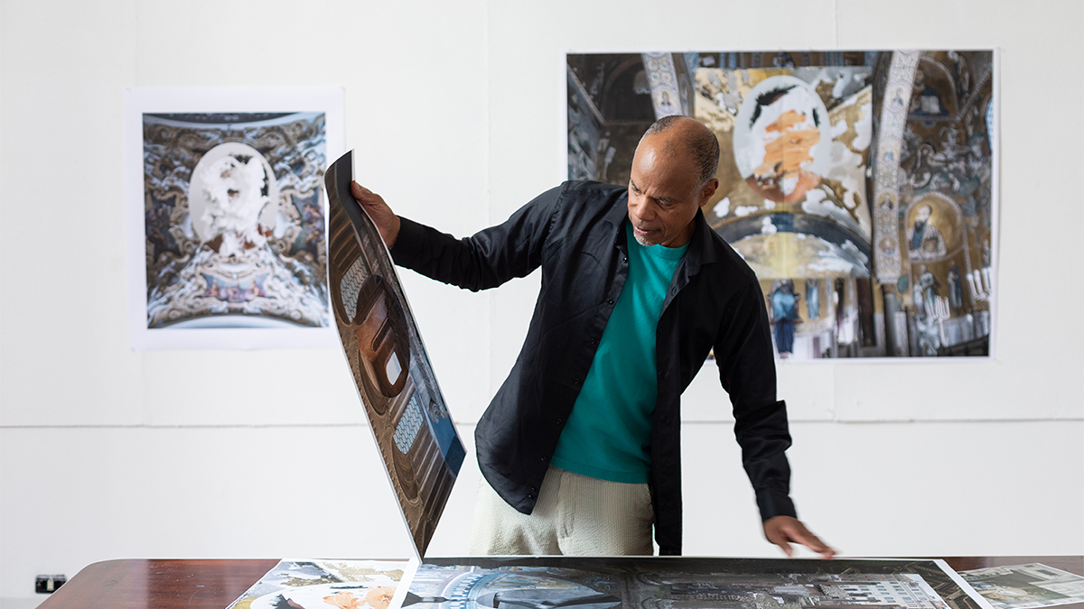Color photograph of a black man in an artist studio looking at his prints