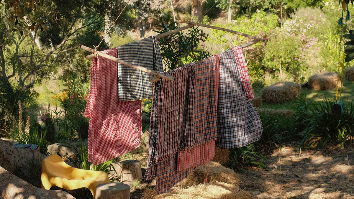 Color photograph of handwoven textiles on a rack placed in a garden landscape