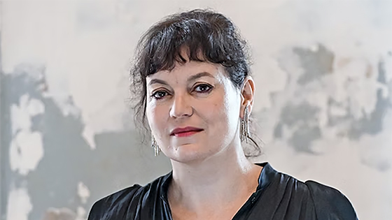 Color photograph of the head and shoulders of a light skinned woman with dark hair smiling slightly at the camera