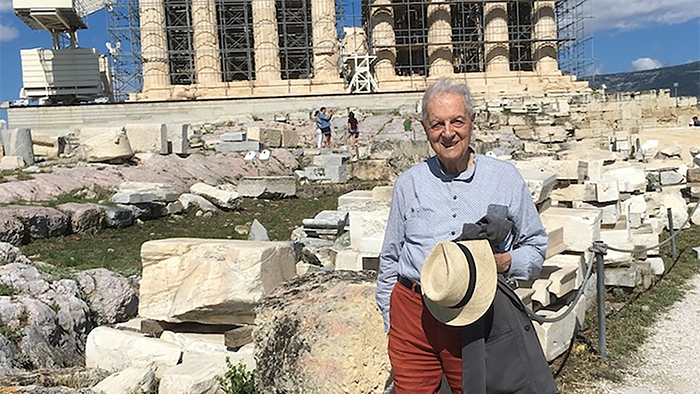 Color photograph of an older, light skinned man standing in front of the Parthenon in Athens