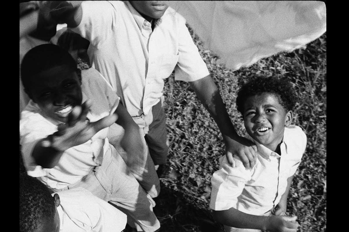 Still from Garrett Bradley's film America showing three small black boys on the grass looking up at the camera