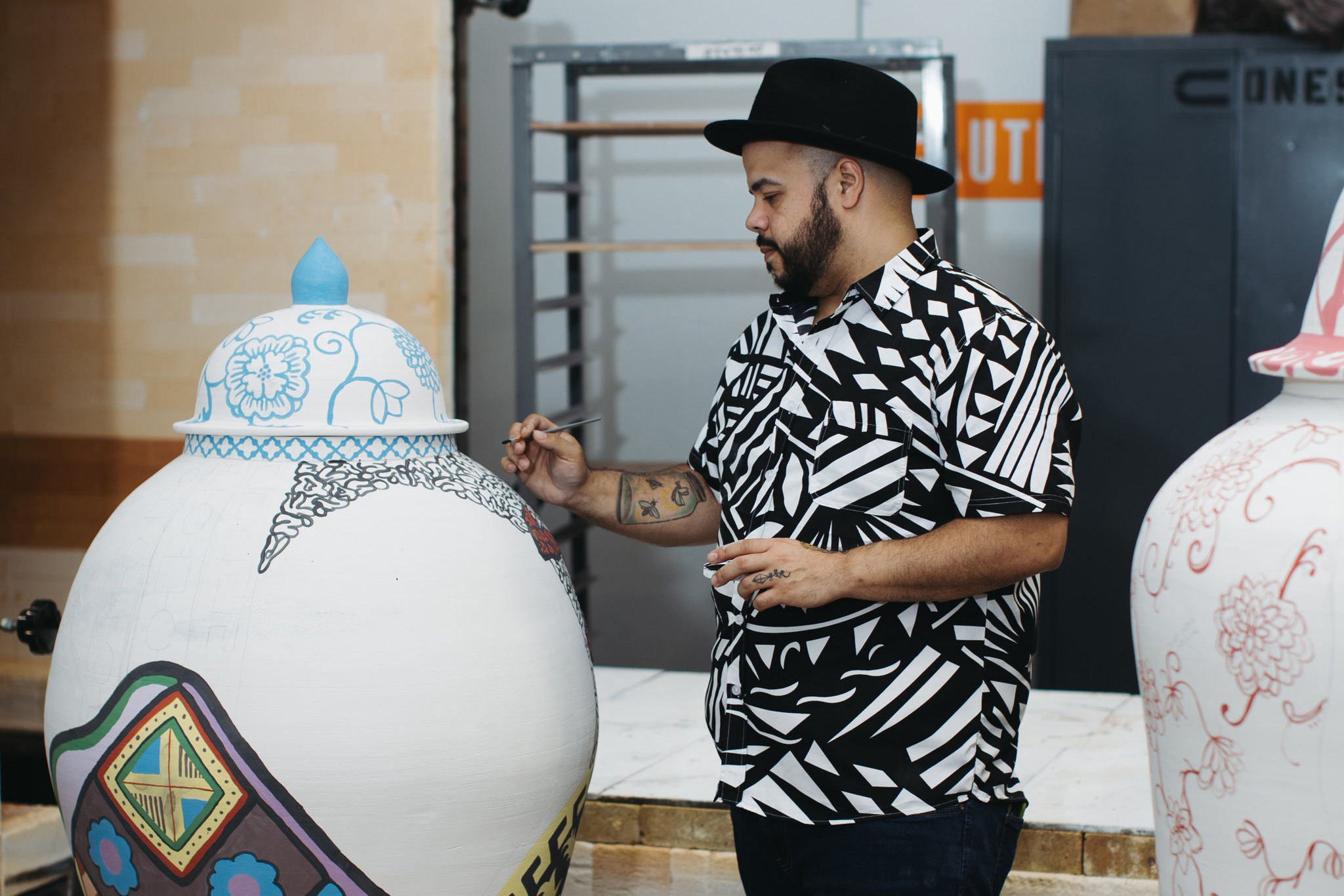 Artist Roberto Lugo hand paints a large white ceramic vase
