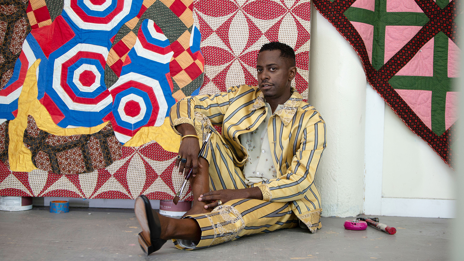 Color photograph of Sanford Biggers, sitting in his studio in front of a quilted work, taken by Lexie Moreland