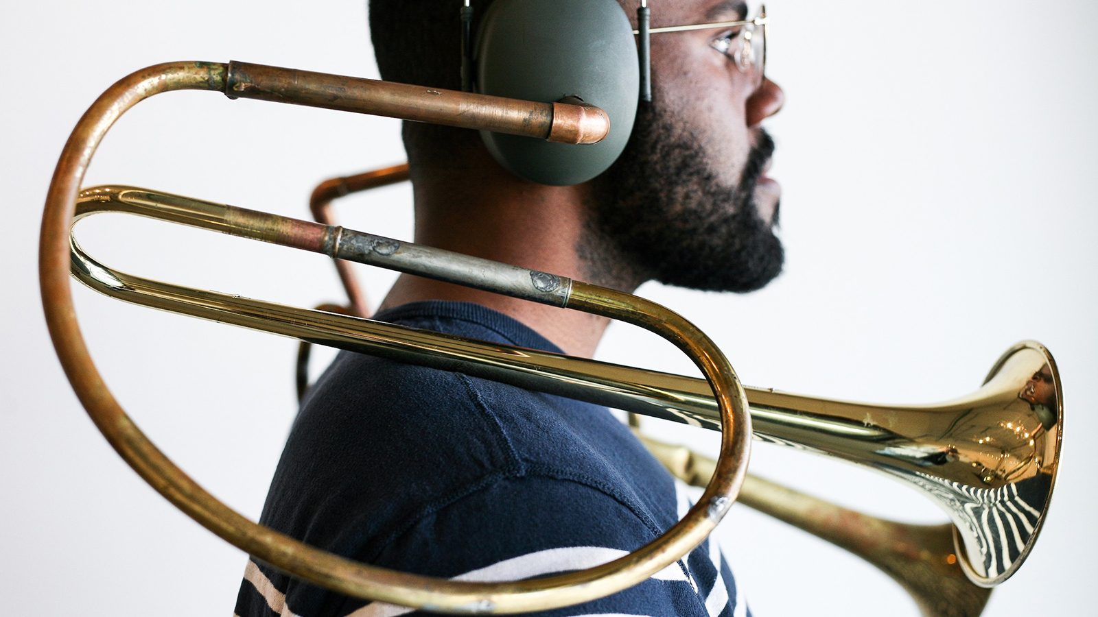 Color profile photograph of a black man wearing a sculptural brass musical instrument on his head