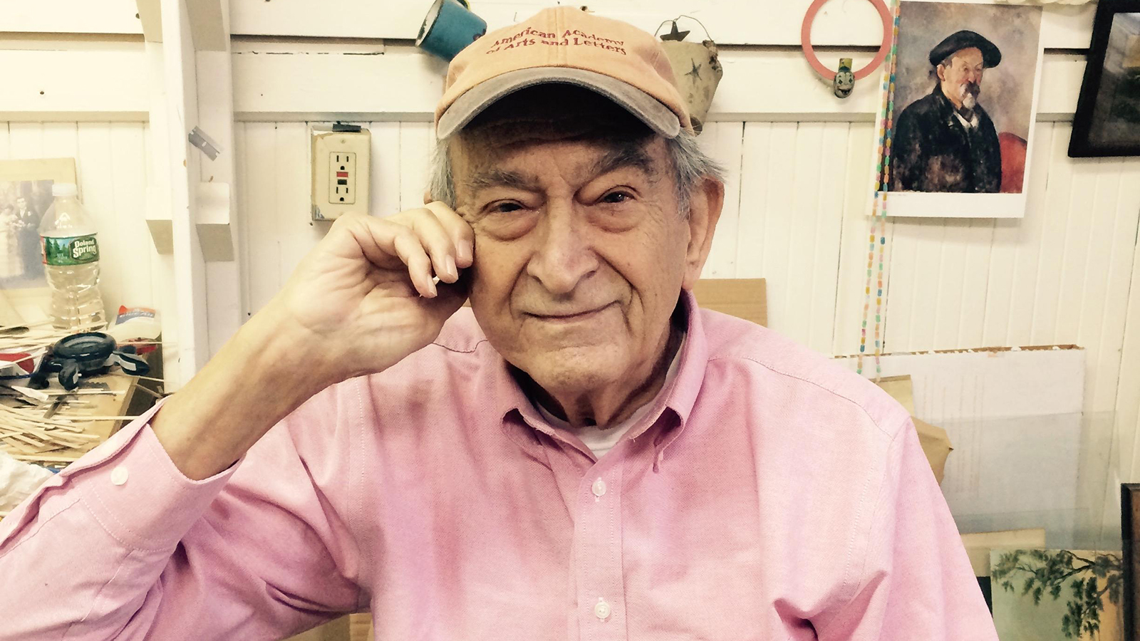 Color photograph of Varujan Boghosian, wearing a pink button-up shirt, at his White River Junction studio in 2017