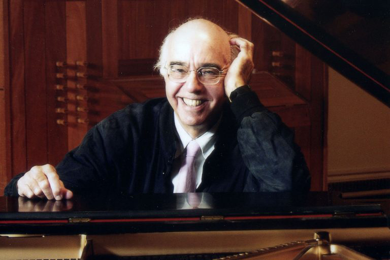 Color photograph of the arms, head, and torso of Yehudi Wyner sitting at a piano