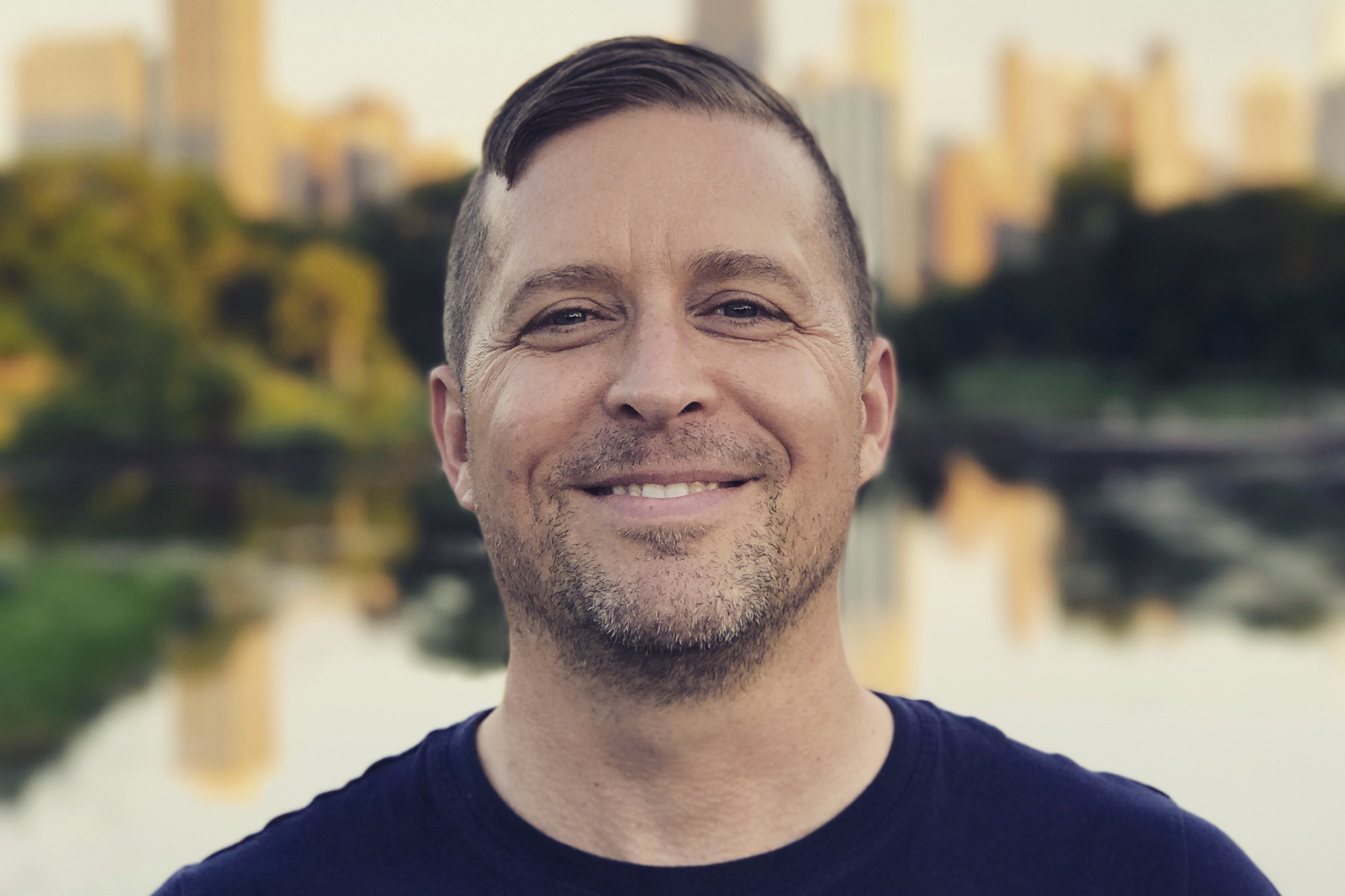 Color portrait of the head and shoulders of Sinclair Bell, in an urban park setting