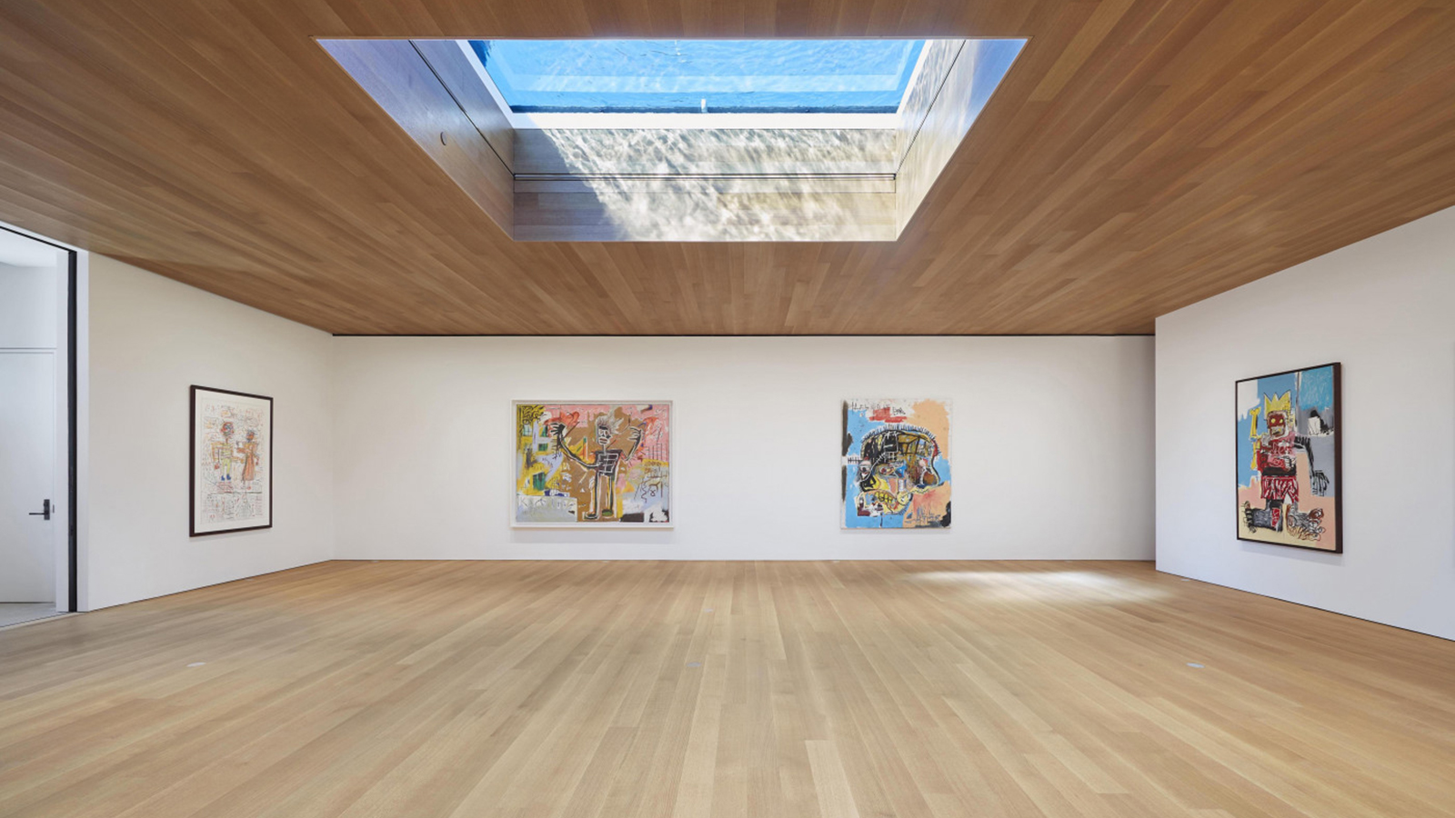 An interior view of the Brant Foundation in New York shows four paintings hanging on three walls, a wood floor in the foreground, and a skylight in the ceiling