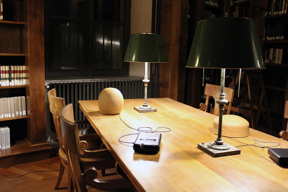 Color photographg of a cassette recorder plugged into a egg shaped ceramic vessel, both sitting on a library table